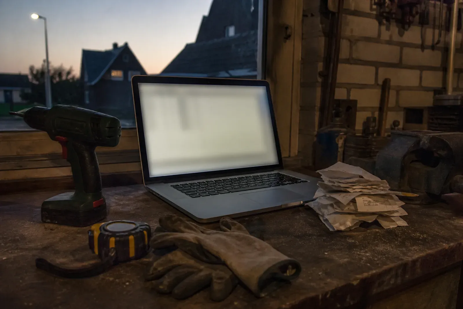 Werkbank in een schuur met een laptop tussen het gereedschap, aan het eind van een werkdag